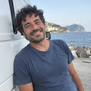 Luca, uomo italiano sui 40, appoggiato a un furgone al mare